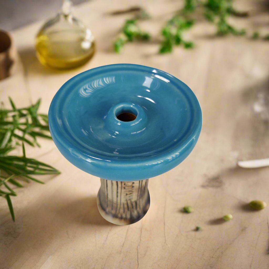 Single-hole Cocoyaya phunnel bowl in blue ceramic, placed on a light surface with herbs and oil in the background, designed for hookah use.